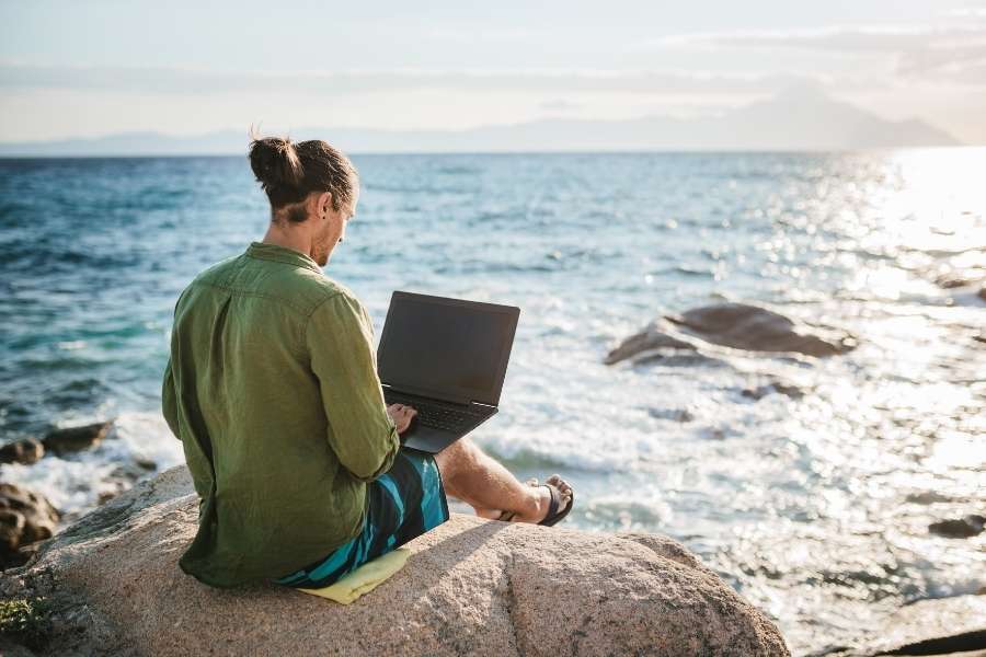 Digital nomad working on laptop by ocean beach managing digital nomad tax planning and compliance