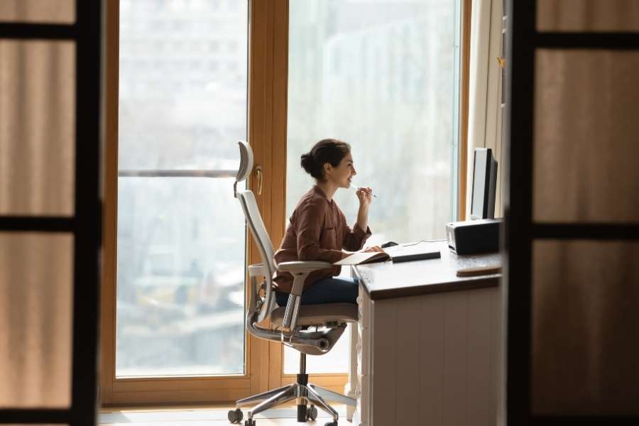 Ergonomic home office with woman working at window desk in natural light setting